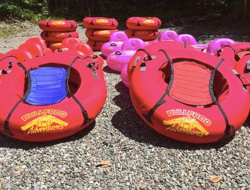A collection of colorful inflatable tubes in red and pink, arranged on a gravel surface, ready for water adventures.