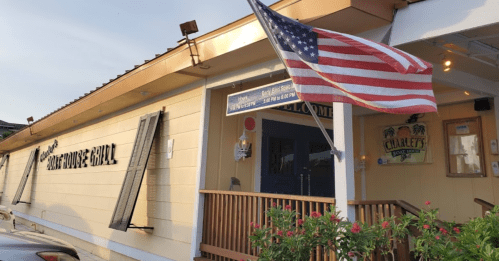Exterior of a restaurant with a welcoming sign and an American flag flying in front, surrounded by flowers.