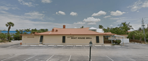 A restaurant building with an orange roof, "Charlie's Boat House Grill" sign, surrounded by palm trees and a parking lot.