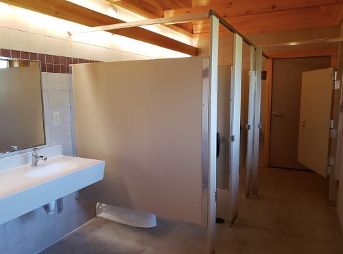 A clean public restroom with three stalls, a sink, and wooden ceiling beams.