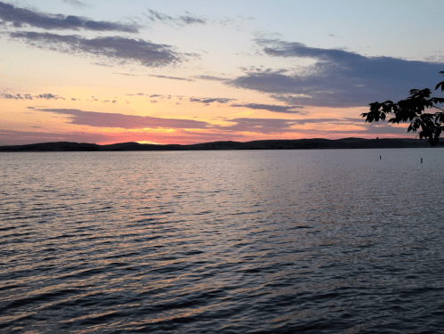 A serene lake at sunset, with colorful clouds reflecting on the water and distant hills silhouetted against the sky.