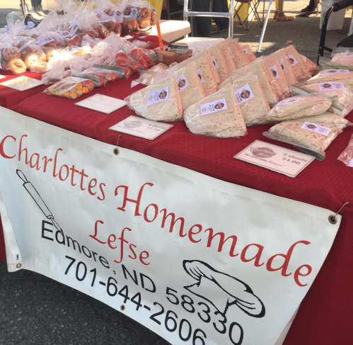 A table at a market displaying homemade lefse, with a sign for "Charlotte's Homemade Lefse" and contact information.