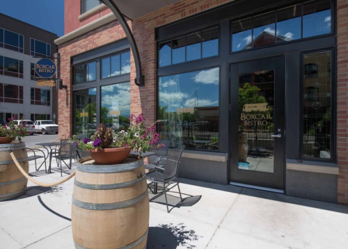 Exterior of Boxcar Bistro with large windows, outdoor seating, and flower planters on a sunny day.
