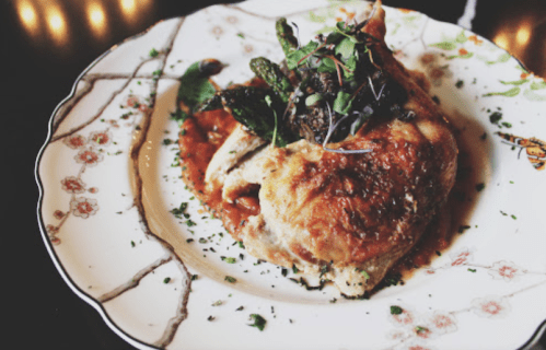 A beautifully plated chicken dish topped with greens and herbs, served on a decorative floral plate.