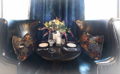 A cozy dining setup with a round table, elegant glassware, and a floral centerpiece in a stylish restaurant booth.