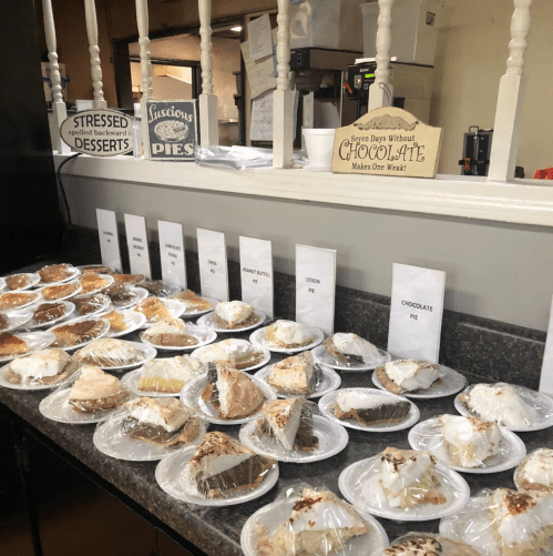 A display of various pies and desserts, each labeled, with a sign about chocolate's importance.