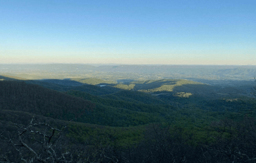 A panoramic view of rolling green mountains and valleys under a clear blue sky during sunset.