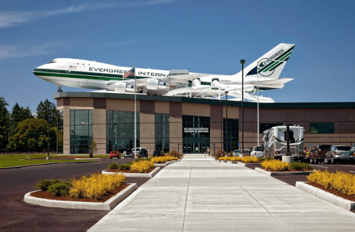 A large airplane model is mounted on a building, with a clear blue sky and landscaped pathway in the foreground.