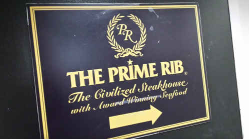 Sign for "The Prime Rib" steakhouse, featuring a logo and text about award-winning seafood, with an arrow pointing left.