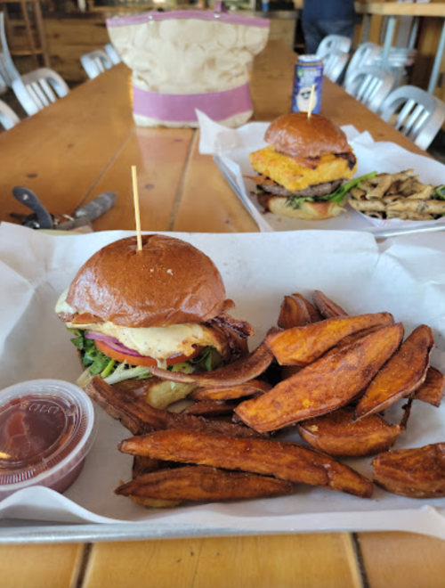 A delicious burger with toppings and a side of crispy sweet potato fries, served with ketchup on a wooden table.