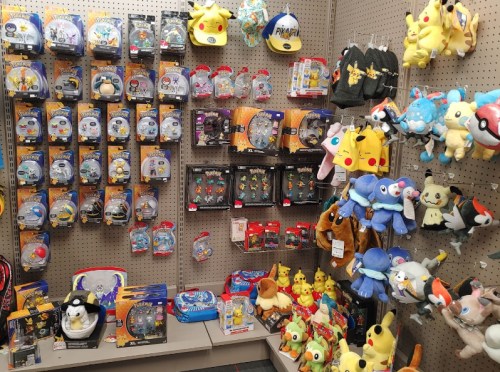 A display of Pokémon merchandise, including toys, plushies, hats, and collectibles on a store shelf.