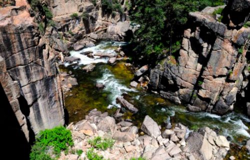 A scenic view of a rocky river canyon with flowing water and lush greenery.