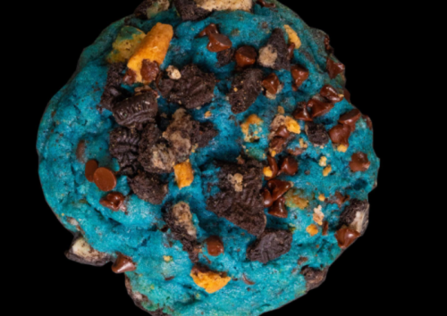 A large, vibrant blue cookie topped with chocolate chips and crushed cookies.