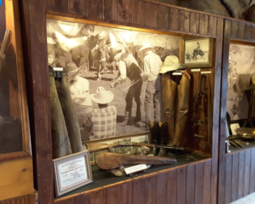 Display of vintage cowboy gear and photographs in a rustic wooden exhibit.