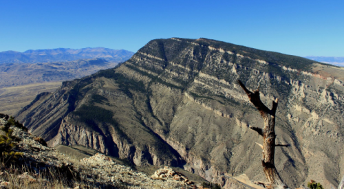 A rugged mountain landscape with layered rock formations and a clear blue sky in the background.