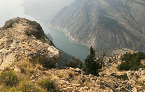 A scenic view from a rocky mountain peak overlooking a winding river and lush green hills in the distance.