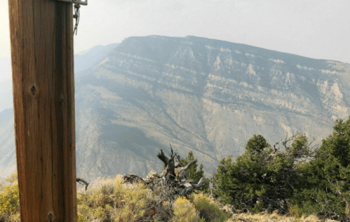 A wooden post stands in the foreground, with a hazy mountain landscape in the background.