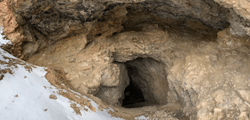 Entrance to a rocky cave, partially covered in snow, with a dark tunnel leading into the interior.