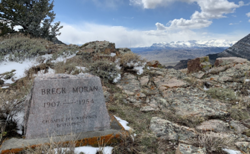 A gravestone for Breck Moran (1907-1954) on a rocky hillside with a mountainous landscape in the background.