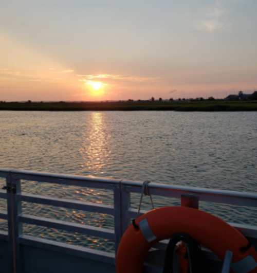 A sunset over calm waters, with a life ring hanging on a boat railing in the foreground.
