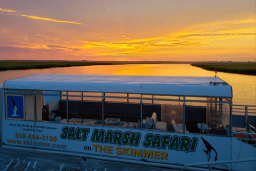 A boat named "The Skimmer" is docked at sunset, with vibrant colors reflecting on the water and marshland in the background.
