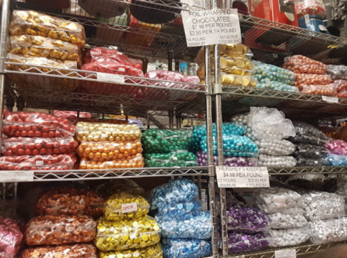 Shelves filled with colorful bags of foil-wrapped chocolates and Hershey's Kisses, with price signs displayed.