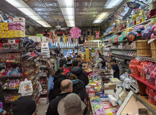 A busy candy store filled with colorful sweets, snacks, and customers browsing the aisles.