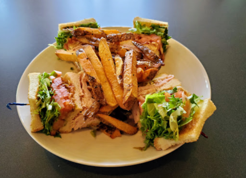 A plate with a club sandwich filled with lettuce, tomato, and turkey, accompanied by a side of golden fries.