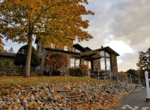 A stone house surrounded by autumn foliage and colorful leaves, with a cloudy sky in the background.