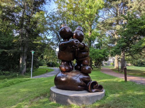 A bronze sculpture of two children holding hands, standing on a large bag, surrounded by greenery.