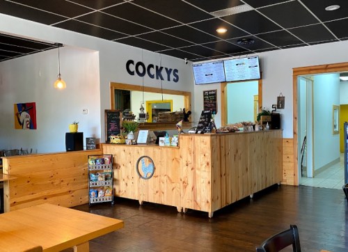 Interior of a cozy restaurant named "Cocky's," featuring a wooden counter and menu boards. Bright and inviting atmosphere.