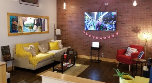 Cozy living room with a sofa, red chair, TV, and decorative elements on a brick wall. Warm and inviting atmosphere.
