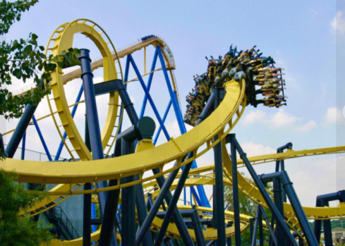 A roller coaster with yellow tracks and a blue structure, featuring riders upside down during a loop.