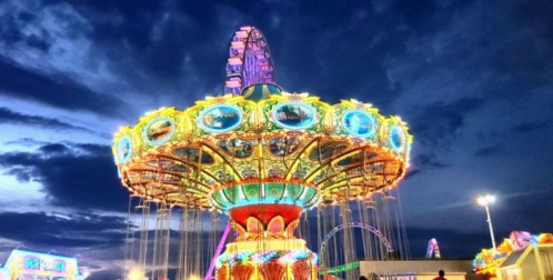 A brightly lit carnival ride against a dramatic evening sky, with colorful lights illuminating the scene.