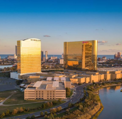 Aerial view of two golden skyscrapers beside a river, with a city skyline and ocean in the background.