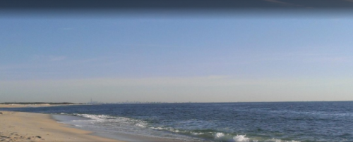 A serene beach scene with gentle waves and a clear sky, featuring a distant city skyline on the horizon.