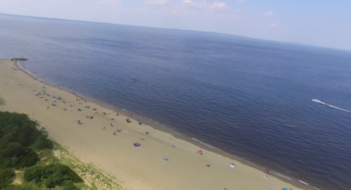 Aerial view of a sandy beach with people relaxing under umbrellas and a calm blue sea in the background.