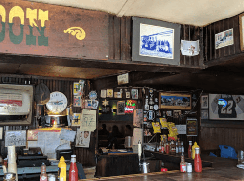 A rustic bar interior with wooden walls, vintage photos, and condiments on the counter.
