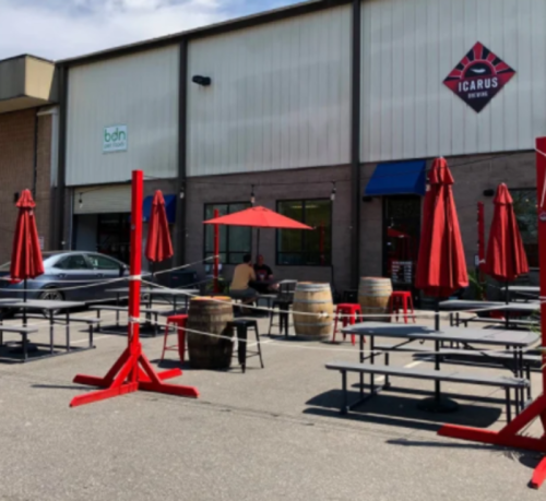 Outdoor seating area with red umbrellas and picnic tables in front of a building labeled "Icarus Brewing."