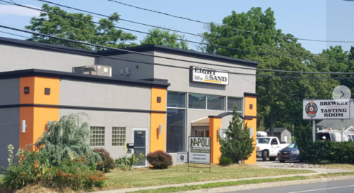A modern building with orange and gray exterior, featuring a sign for a brewery and tasting room nearby.