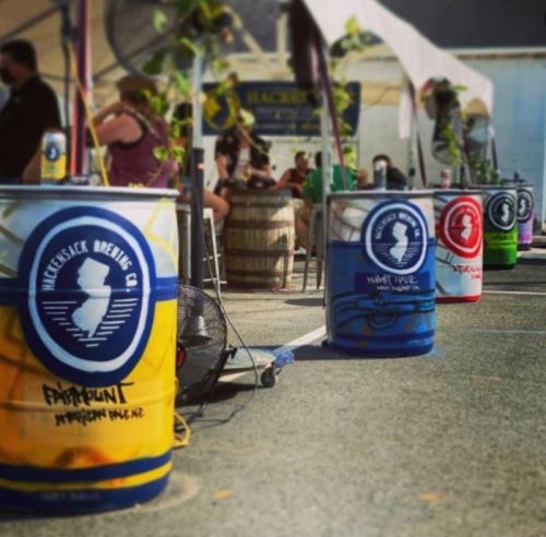 Colorful barrels from Hackensack Brewing Co. line an outdoor event space, with people enjoying the atmosphere in the background.