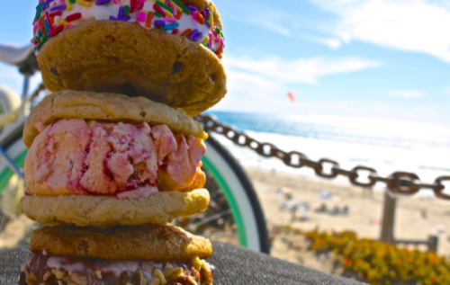 A stack of colorful ice cream sandwiches with a beach and ocean in the background on a sunny day.