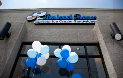 Sign for "The Baked Bear" ice cream sandwich shop, with blue and white balloons outside the entrance.