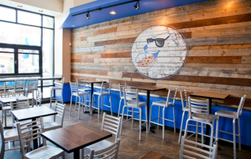 Cozy café interior with wooden wall art, blue accents, and empty tables and chairs.
