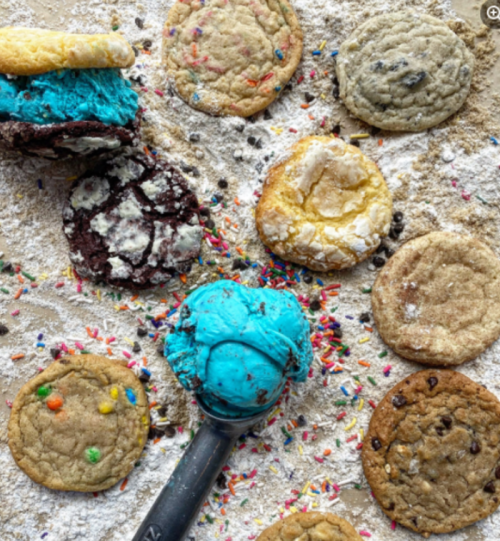 A variety of cookies scattered on a surface with flour and colorful sprinkles, alongside a scoop of blue ice cream.