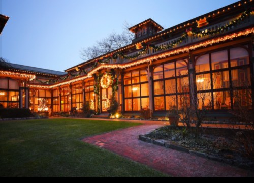 A beautifully lit building decorated with holiday lights and wreaths, surrounded by a well-maintained garden at dusk.