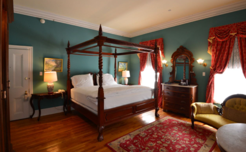 A cozy bedroom featuring a four-poster bed, elegant decor, and warm lighting with a vintage armchair and wooden furniture.