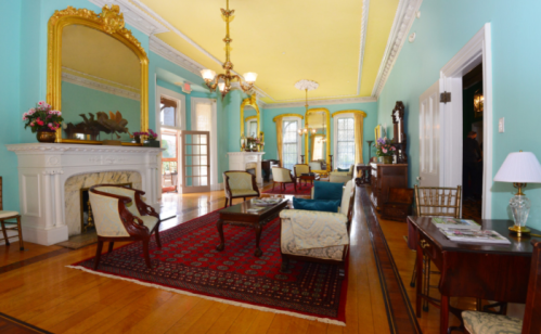 Elegant room with turquoise walls, yellow ceiling, ornate mirrors, vintage furniture, and a decorative fireplace.