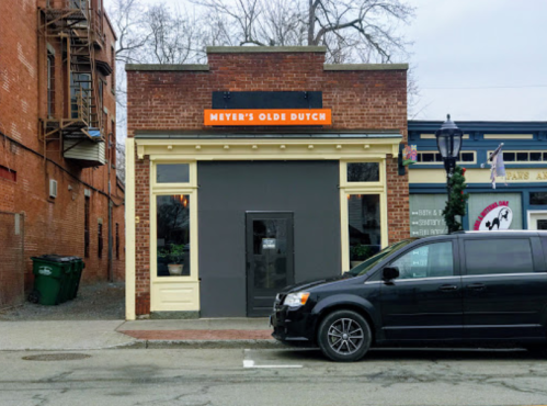 A brick building with a sign reading "Meyer’s Olde Dutch," parked black van, and nearby trash bins.