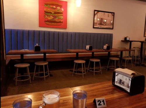 A cozy restaurant interior with blue seating, wooden tables, and a colorful burger artwork on the wall.